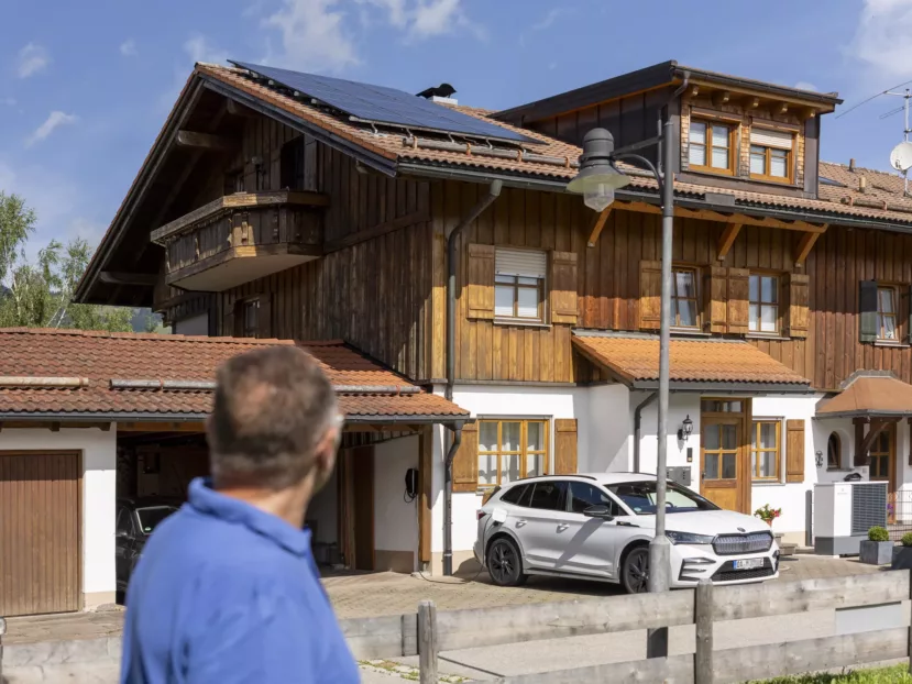 Aufnahme eines Hauses mit Photovoltaikanlage auf dem Dach und einem E-Auto in der Einfahrt sowie einer Wärmepumpe neben der Haustüre.